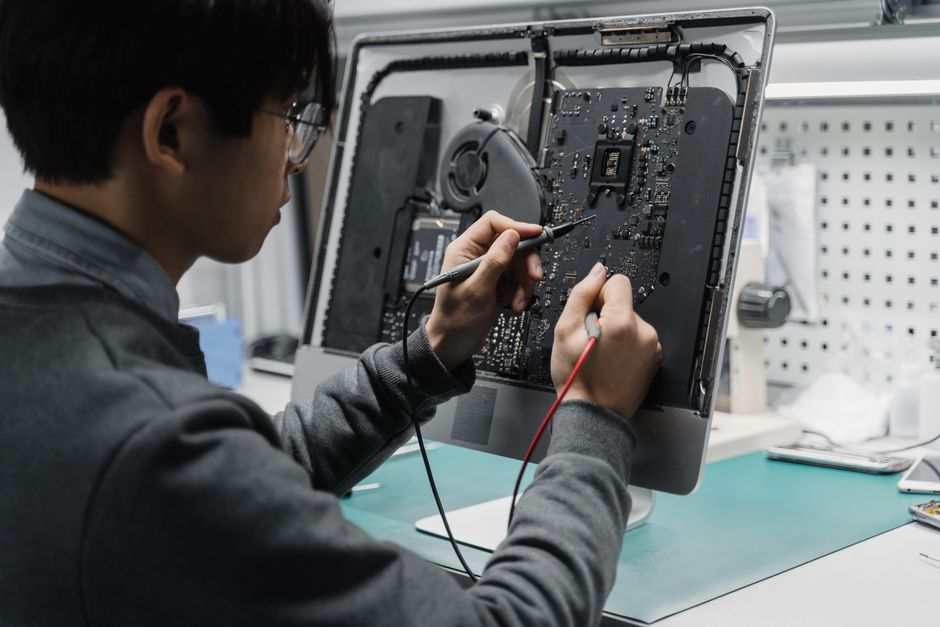 A technician works on a computer motherboard using tools at a workspace, focusing on electronics repair