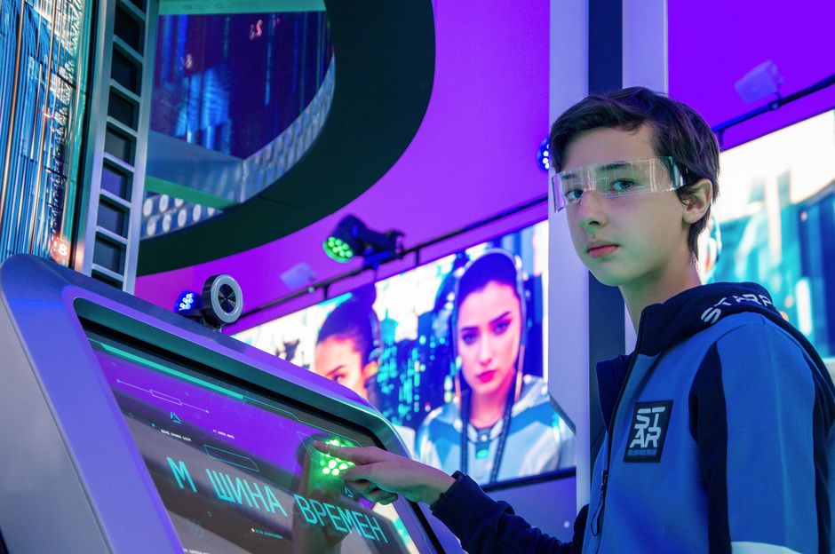Teen boy in a digital room interacting with a futuristic touchscreen device wearing protective goggles